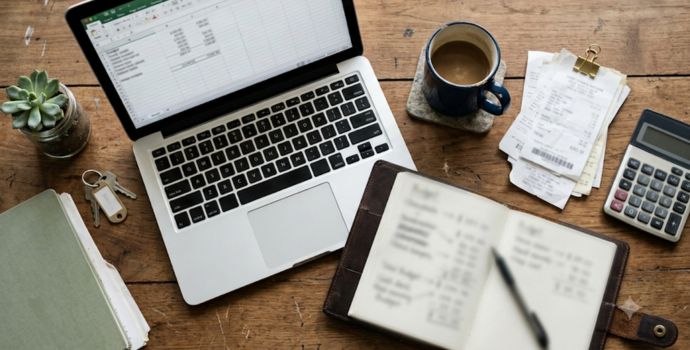 Flat-lay desk setup for small business budgeting with laptop, receipts, and calculator
